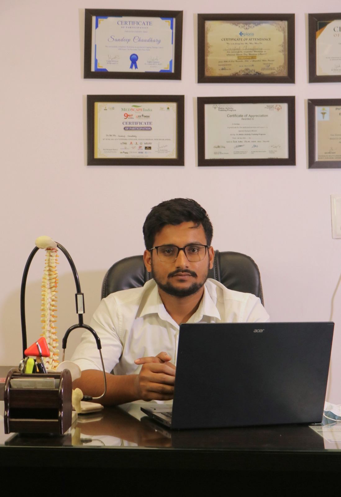 Dr. Sandeep Chaudhry at his desk below his certifications wall